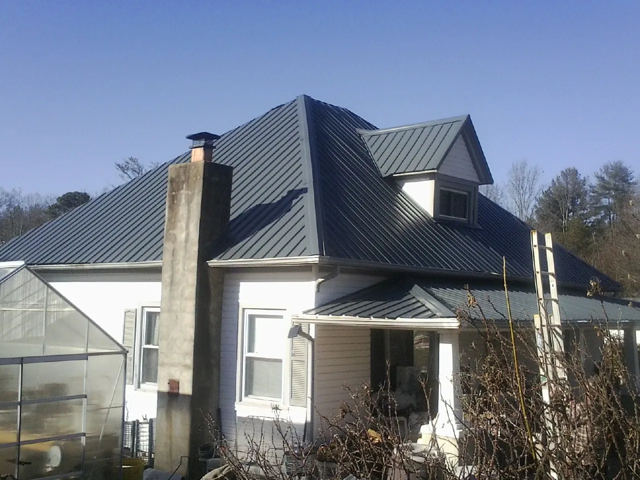Dark blue standing seam metal roof on a white farmhouse with dormer — Slate & Tile Roof Repair by Roofing Brothers in Cement City