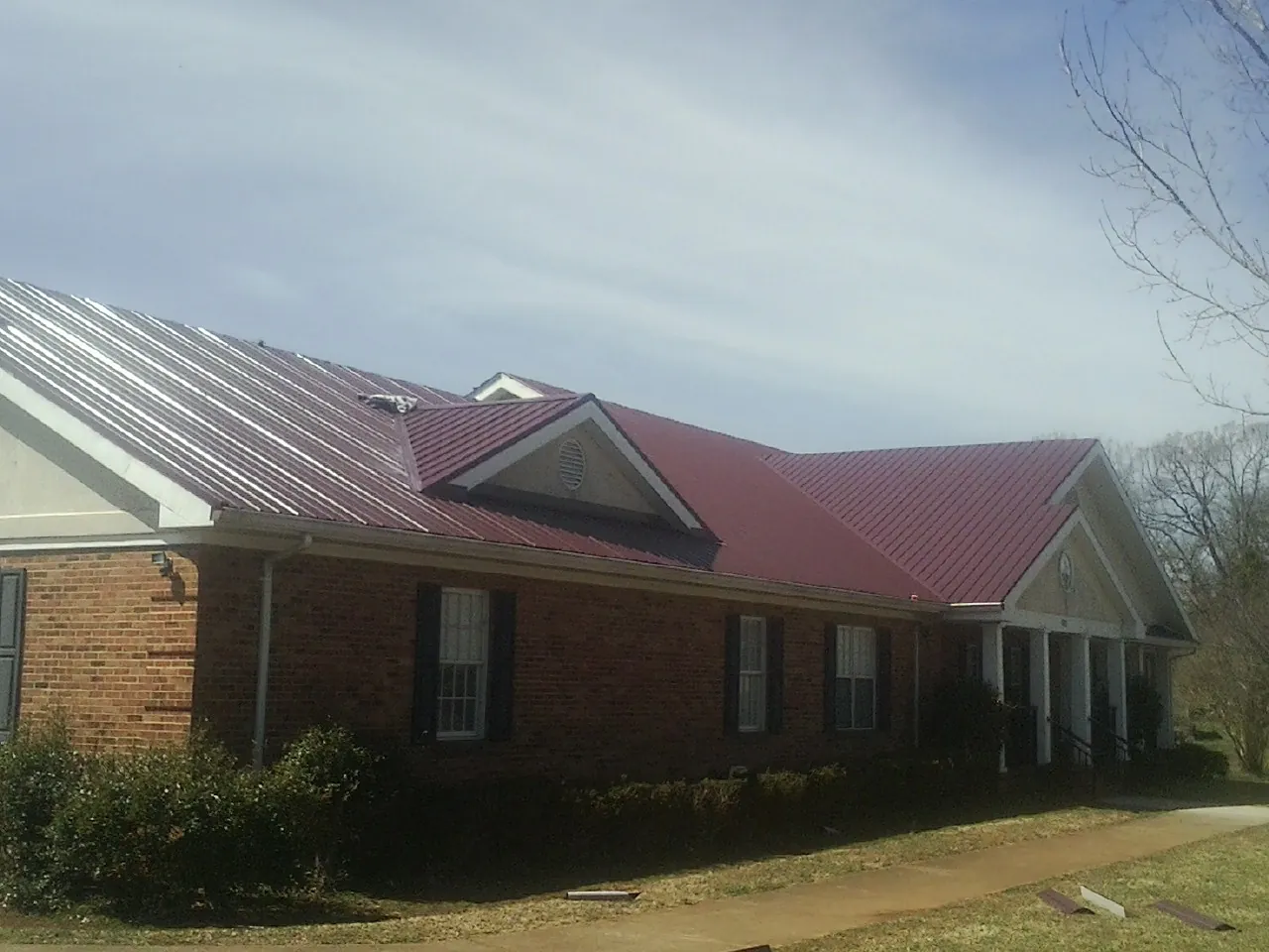 Red metal roof with gabled entries on a long brick building, from a Hail Damage Roof Repair job in Cement City