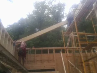 Carpenter raising a rafter beam on a new second story frame in Cement City