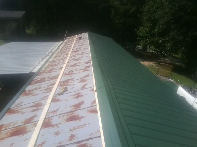 Old rusted panels beside newly installed green metal roofing — Wind Damage Roof Repair by Roofing Brothers in Cement City