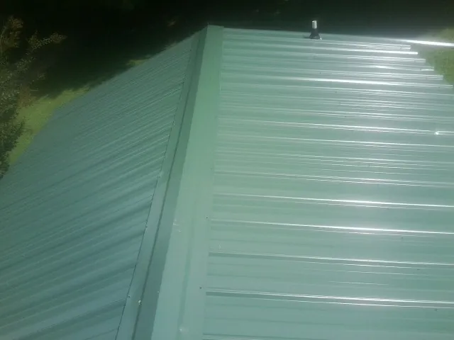 New green metal panels meeting at the ridge of a roof — Flat Roof Repair work by our crew in Cement City