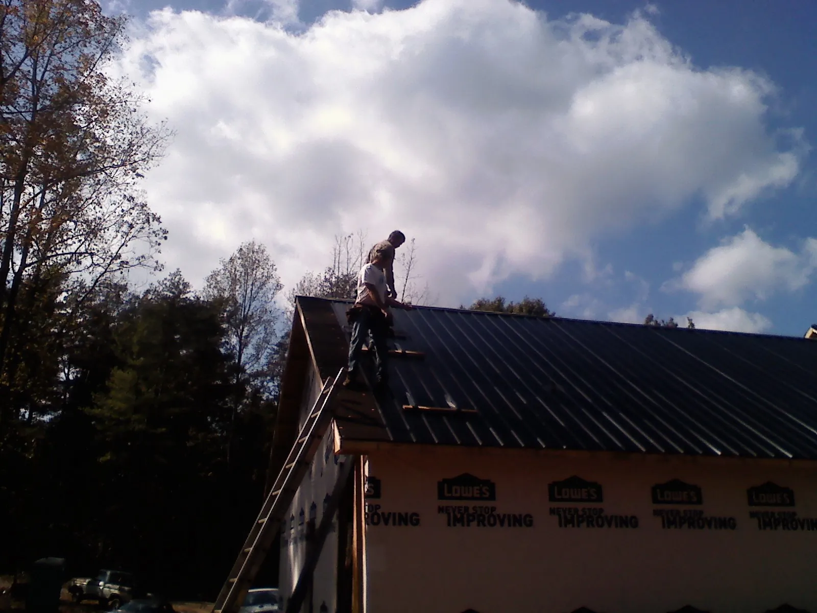 Roofer fastening dark metal panels high against a cloudy sky, from a Roof Inspection job in Cement City