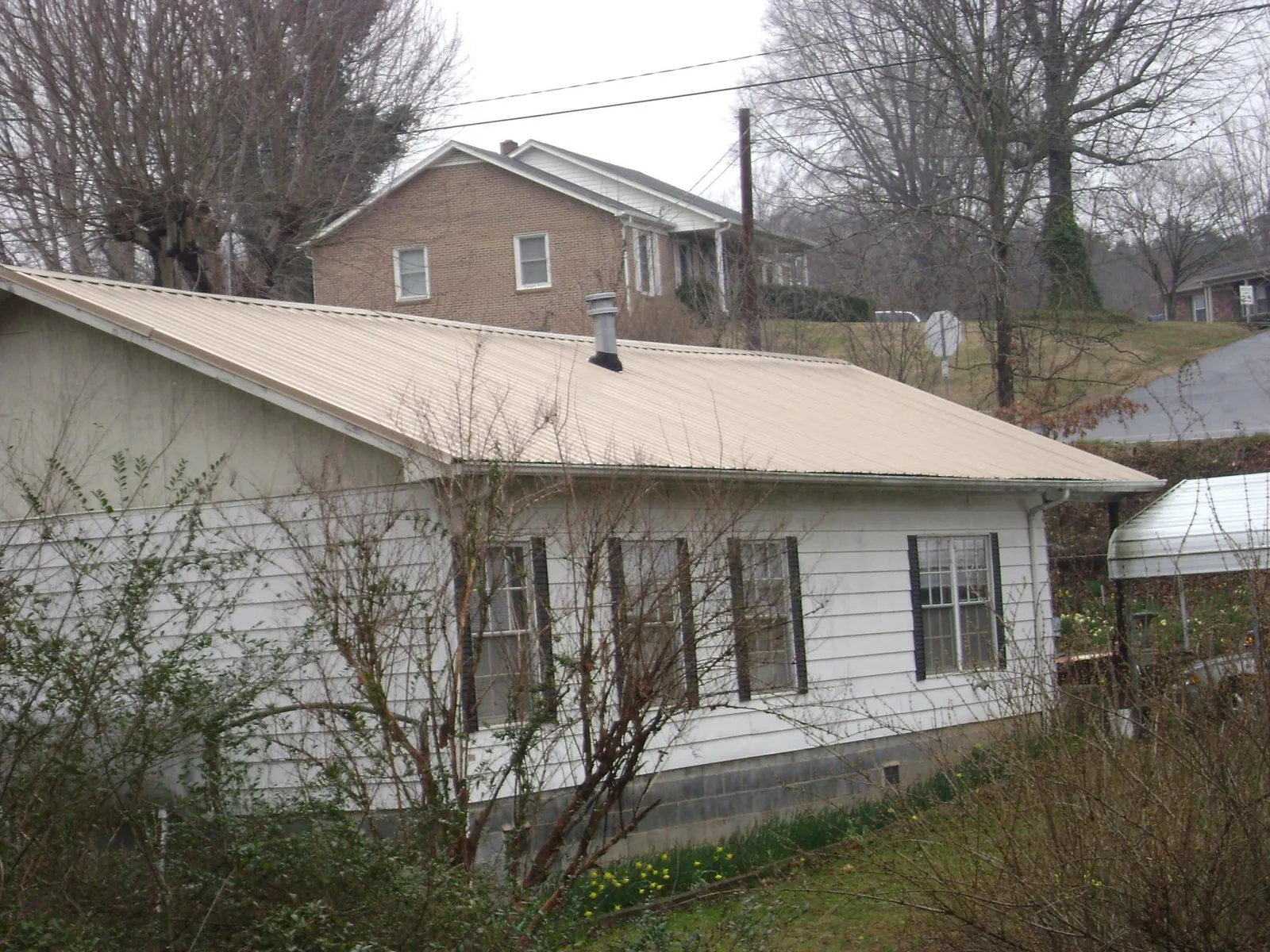 Tan metal roof on a white sided house set into a hillside — Commercial Roofing by Roofing Brothers in Cement City