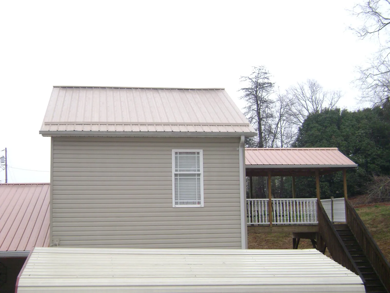 Tan metal roofs on a two story addition and attached porch, from a Roof Replacement job in Cement City